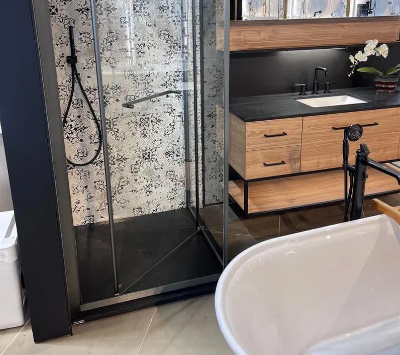 Douche vitrée sur base noire, derrière une baignoire autoportante