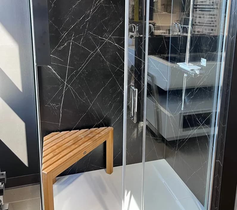 Douche vitrée sur base blanche, avec banc en bois et murs noirs veinés