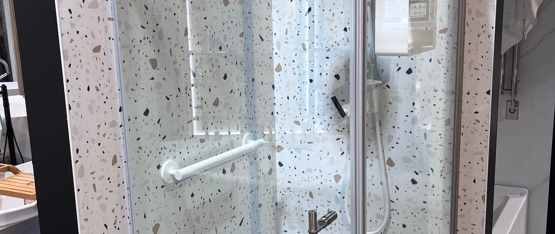 Douche vitrée aux murs effet terrazzo, avec barre d’appui